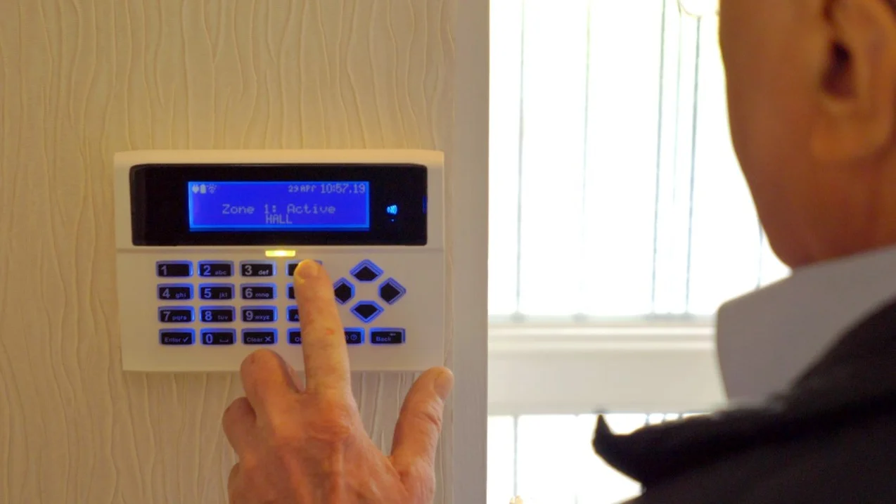 An individual activating a modern home security alarm system with a sleek keypad and bright blue display reading 'Zone 1: Active,' perfectly highlighting the advanced residential safety solutions offered by Bolton security companies.